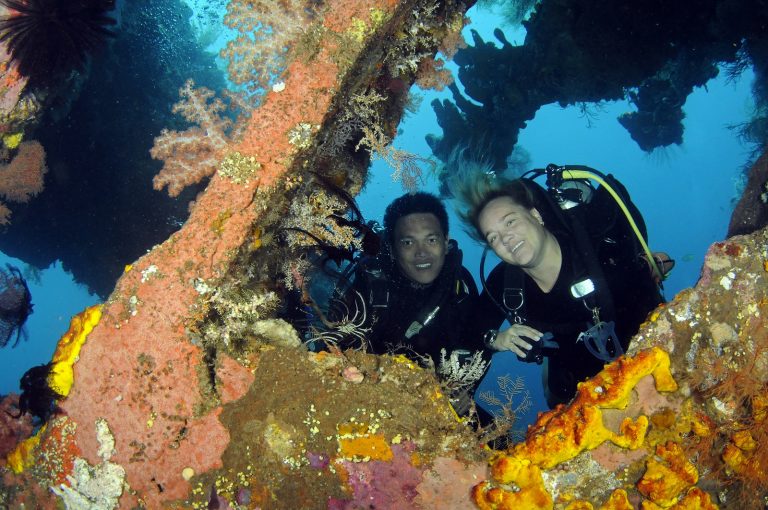 Minni Vangsgaard, Platinum PADI Course Director, scuba diving with another diver near a colorful coral reef in Bali, Indonesia.
